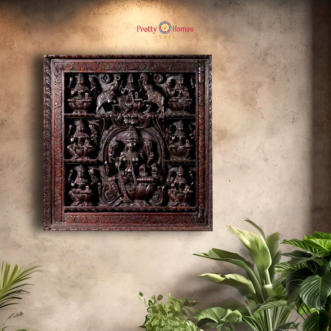 A carved wooden wall panel featuring the Hindu goddess of wealth and prosperity, Lakshmi, in a decorative setting with plants around it.