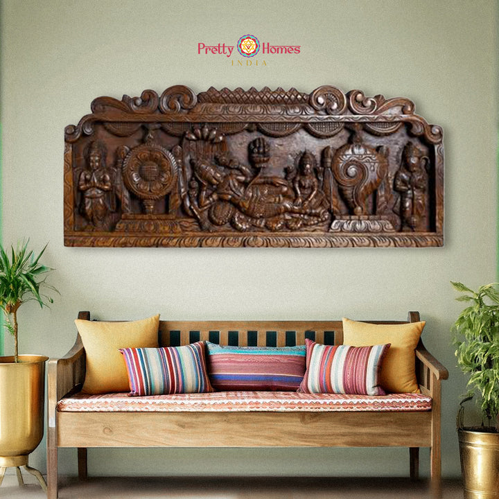 Decorative wooden wall panel with intricate carvings above a wooden bench with colorful cushions on a light green wall.