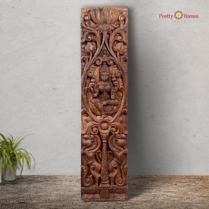 A vertical wooden panel featuring intricate carvings of the goddess Lakshmi surrounded by lotuses and Yalis, with a polished finish.