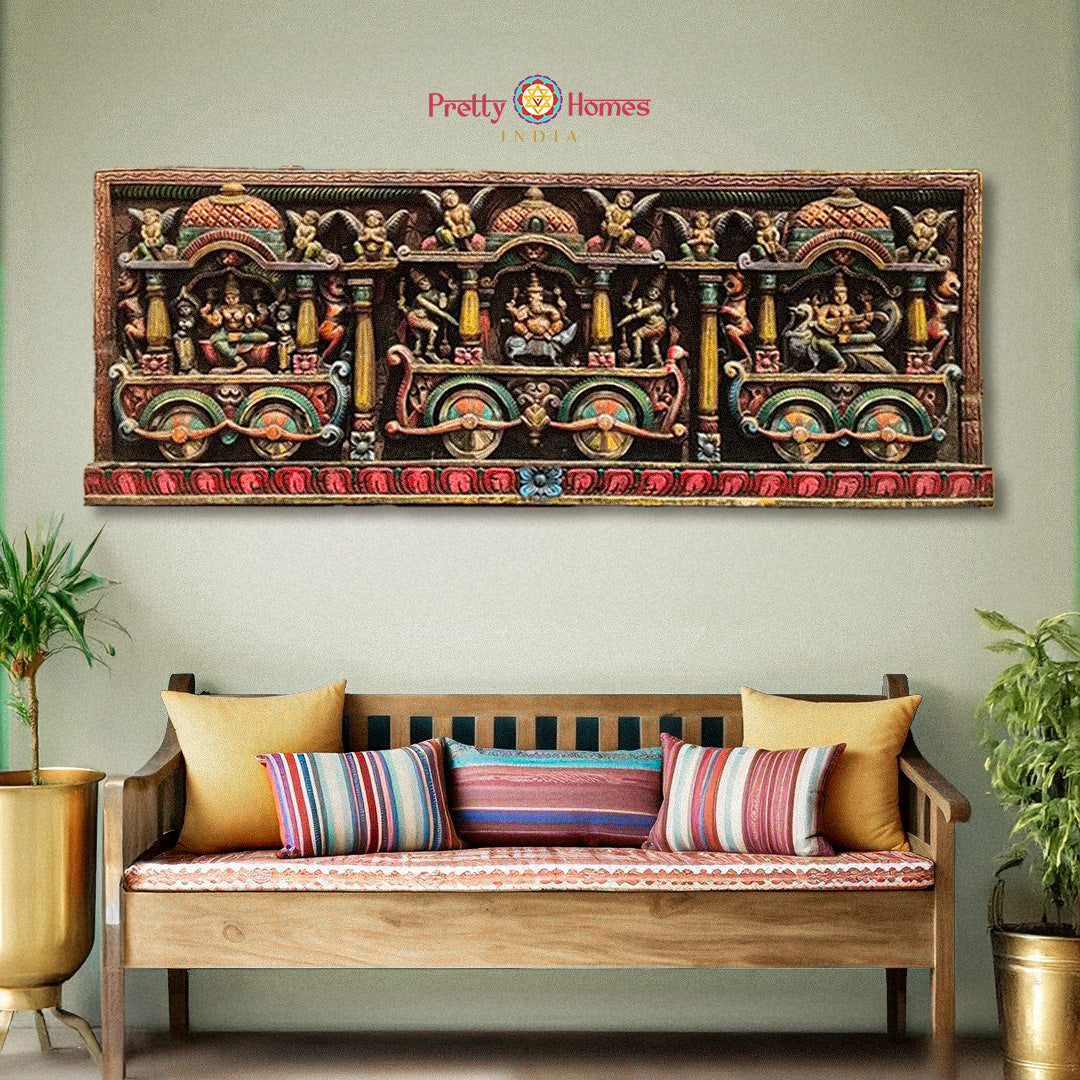 Colorful carved wooden panel featuring Ganesh, Laxmi, and Saraswati above a sofa