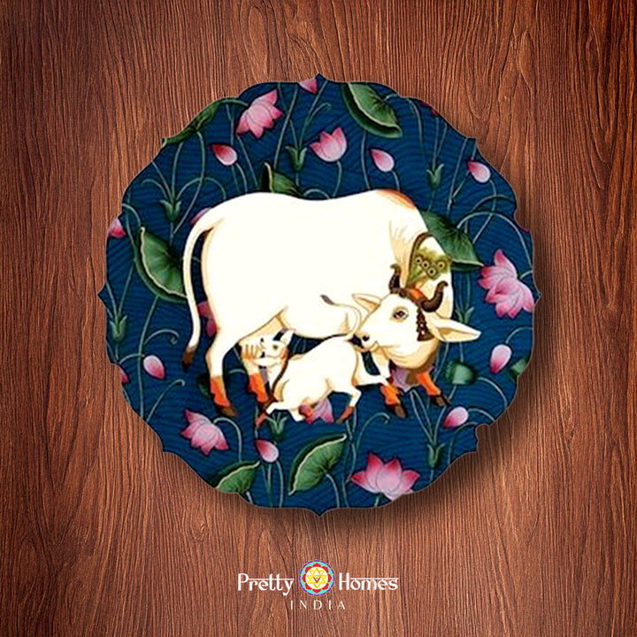Petal-shaped handpainted pichwai wall plate featuring a white cow with calf and lotus flowers on a dark blue background.